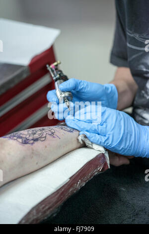 Tattoo-Künstler mit blauen Latex Handschuhen Tätowierungen eine Bio-mechanische Bilder auf Kunden-arm Stockfoto