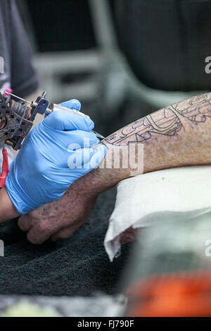 Tattoo-Künstler mit blauen Latex Handschuhen Tätowierungen eine Bio-mechanische Bilder auf Kunden-arm Stockfoto