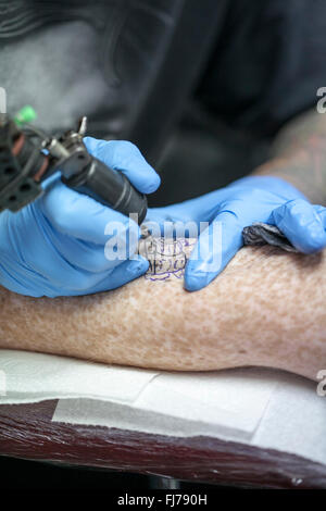 Tattoo-Künstler mit blauen Latex Handschuhen Tätowierungen eine Bio-mechanische Bilder auf Kunden-arm Stockfoto