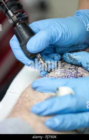 Tattoo-Künstler mit blauen Latex Handschuhen Tätowierungen eine Bio-mechanische Bilder auf Kunden-arm Stockfoto