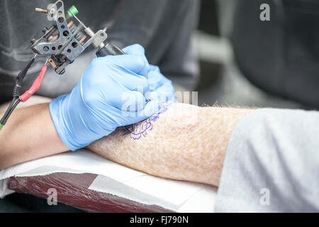 Tattoo-Künstler mit blauen Latex Handschuhen Tätowierungen eine Bio-mechanische Bilder auf Kunden-arm Stockfoto