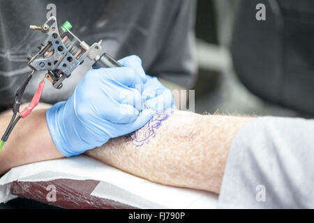 Tattoo-Künstler mit blauen Latex Handschuhen Tätowierungen eine Bio-mechanische Bilder auf Kunden-arm Stockfoto