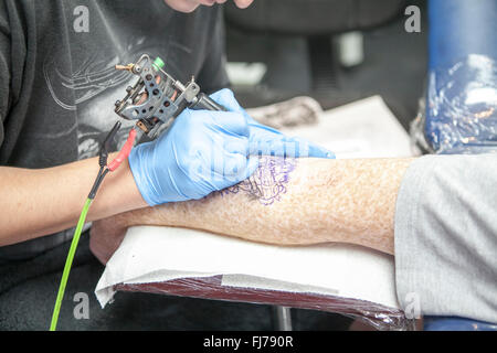 Tattoo-Künstler mit blauen Latex Handschuhen Tätowierungen eine Bio-mechanische Bilder auf Kunden-arm Stockfoto