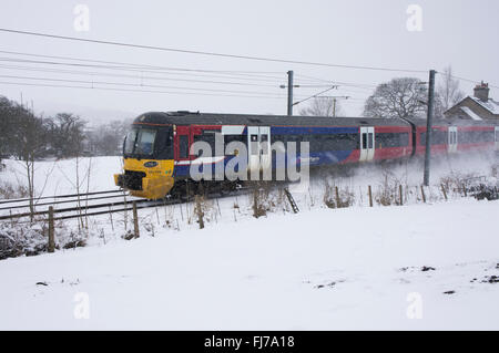 Pendlerzug 333 (Motor, Reisebusse) auf Bahngleisen auf dem Land, Schnee fällt an kalten verschneiten Wintertagen - Burley in Wharfedale, West Yorkshire UK. Stockfoto