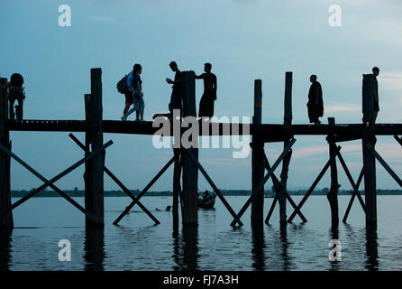 AMARAPURA, Myanmar – die U Bein Bridge erstreckt sich über den Taungthaman Lake bei Mandalay. Die 1,2 Kilometer lange Teakholzkonstruktion, die vermutlich die älteste und längste Teakholzbrücke der Welt ist, ist vom Himmel her umrahmt. Einheimische Fußgänger und Mönche überqueren die Brücke, während Touristen die berühmte Szene beobachten, die besonders bei Sonnenuntergang beliebt ist. Stockfoto