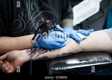 Tattoo-Künstler mit blauen Latex Handschuhen Tätowierungen eine Bio-mechanische Bilder auf Kunden-arm Stockfoto