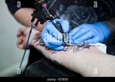 Tattoo-Künstler mit blauen Latex Handschuhen Tätowierungen eine Bio-mechanische Bilder auf Kunden-arm Stockfoto