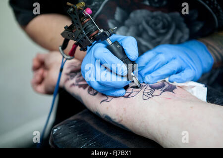 Tattoo-Künstler mit blauen Latex Handschuhen Tätowierungen eine Bio-mechanische Bilder auf Kunden-arm Stockfoto