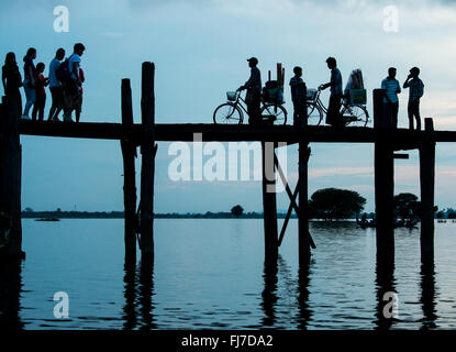 AMARAPURA, Myanmar – die U Bein Bridge erstreckt sich über den Taungthaman Lake bei Mandalay. Die 1,2 Kilometer lange Teakholzkonstruktion, die vermutlich die älteste und längste Teakholzbrücke der Welt ist, ist vom Himmel her umrahmt. Einheimische Fußgänger und Mönche überqueren die Brücke, während Touristen die berühmte Szene beobachten, die besonders bei Sonnenuntergang beliebt ist. Stockfoto