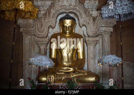 Gautama Buddha Statue Htilominlo Tempel Nyaung-U Myanmar // NYAUNG-U, Myanmar – Eine goldene Statue von Gautama Buddha steht im Htilominlo Tempel, einem der prominenten buddhistischen Tempel in der antiken Stadt Bagan. Der Tempel Htilominlo wurde Anfang des 13. Jahrhunderts während der Regierungszeit von König Htilominlo erbaut und repräsentiert den architektonischen Stil der späten Bagan-Zeit. Der Tempel ist bekannt für seine gut erhaltenen Fresken und mehrere Buddha-Bilder, die in seinen Innenräumen untergebracht sind. Nyaung-U dient als Tor zur archäologischen Zone Bagan, die Tausende von buddhistischen Tempeln beherbergt Stockfoto