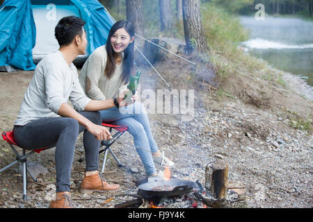 Junge chinesische Paare sitzen neben Lagerfeuer zubereiten Stockfoto