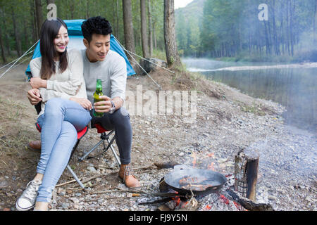 Junge chinesische Paare sitzen neben Lagerfeuer zubereiten Stockfoto