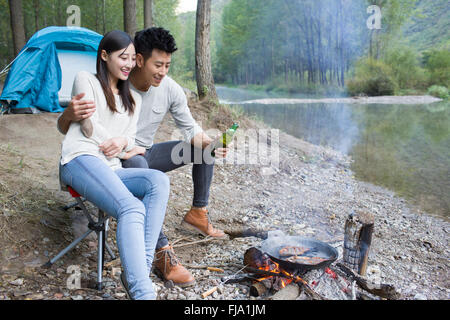 Junge chinesische Paare sitzen neben Lagerfeuer zubereiten Stockfoto