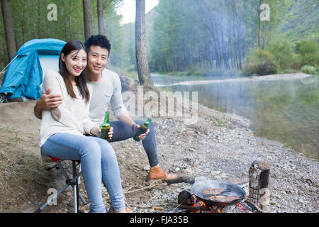 Junge chinesische Paare sitzen neben Lagerfeuer zubereiten Stockfoto