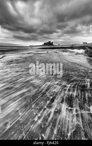 Bamburgh Castle von der felsigen Küste gesehen. Eine relativ lange Belichtungszeit ermöglichte die Wellen zu Streifen Stockfoto