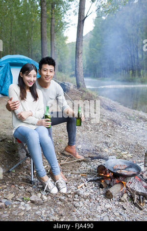 Junge chinesische Paare sitzen neben Lagerfeuer zubereiten Stockfoto