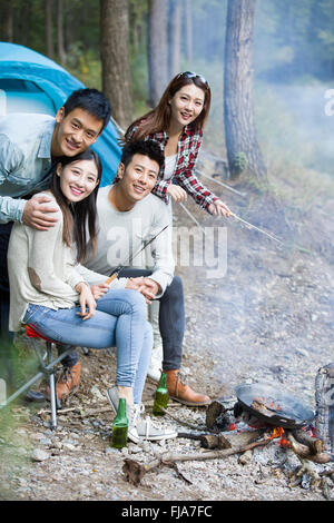 Junge chinesische Freunde sitzen neben Lagerfeuer zubereiten Stockfoto