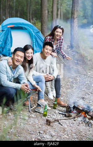 Junge chinesische Freunde sitzen neben Lagerfeuer zubereiten Stockfoto