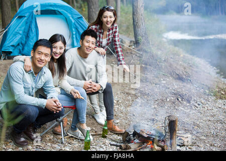 Junge chinesische Freunde sitzen neben Lagerfeuer zubereiten Stockfoto