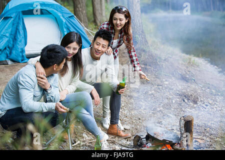 Junge chinesische Freunde sitzen neben Lagerfeuer zubereiten Stockfoto