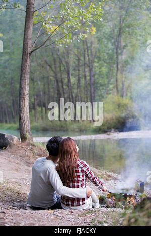 Junge chinesische Paare sitzen neben Lagerfeuer zubereiten Stockfoto