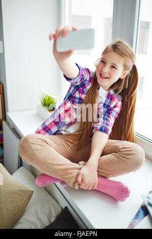 Ziemlich junges Mädchen mit Handy machen ihr Selfie auf Fensterbank Stockfoto