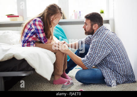 Teenager-Mädchen weint, während ihr Vater ihr beruhigend Stockfoto