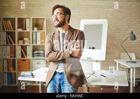 Junge Unternehmer stehen in der Nähe seines Arbeitsplatzes und denken Stockfoto