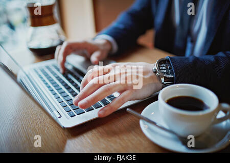 Nahaufnahme von männlichen Händen tippen auf Laptop während der Kaffeepause Stockfoto