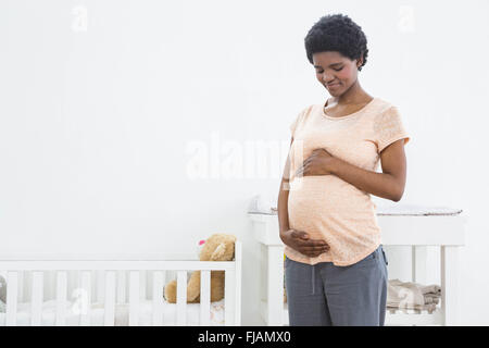Schwangere Frau in der Nähe von Wiege stehen und blickte auf den Bauch Stockfoto