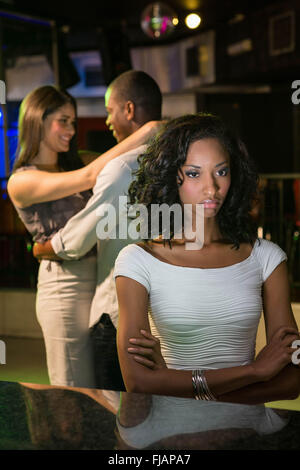 Unglückliche Frau sitzt am bar-Theke und Paare tanzen hinter ihr Stockfoto