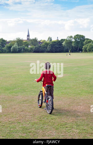 London, Hampstead, Hampstead Garden Vorort, EIN Junge mit seinem Fahrrad in Hampstead Heath Park Erweiterung, Sommertag, blauer Himmel, Turm der St. Jude's Kirche Stockfoto