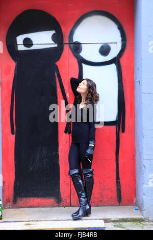 Eine Frau mit einer Zigarette neben Graffiti in Hoxton, London Stockfoto