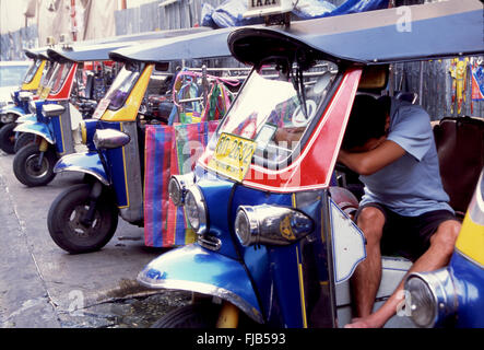 Thailand, Bangkok. Ein erschöpfter Tuk-Tuk-Taxifahrer schlief auf einem Rastanschlag am Steuer seines Fahrzeugs ein Stockfoto