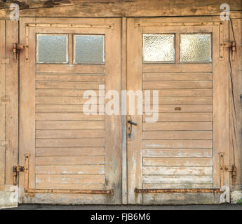 Alt, hellbraun, schmutzig und verwittert Holz Garagentor mit vier kleinen Glasfenstern und verrostet eiserne Beschläge. Stockfoto