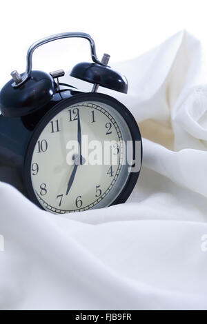 Erwachen-Konzept. Schwarze Wecker auf weißen Laken im Bett Stockfoto