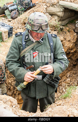 WW2re-enactment. Sie suchen bei der Deutschen Waffen-SS Storm Trooper im Graben der Fixierung eines stick Grenade, stielhandgranate. Iron Cross Band auf der Brust befestigt Stockfoto