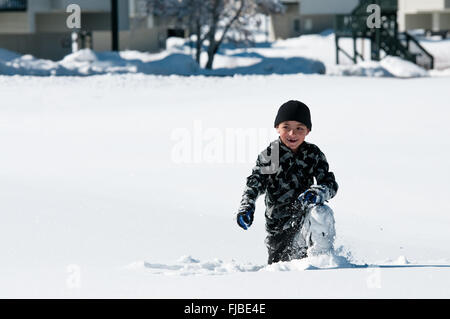 Entzückende kleine Junge kniend im Schnee spielen. Stockfoto