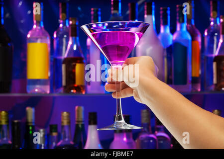 Cocktailglas in Frauenhand mit Bar auf Rückseite Stockfoto