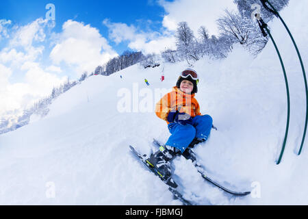 Kleiner junge Skifahrer sitzen mit Ski im Schnee ruhen Stockfoto