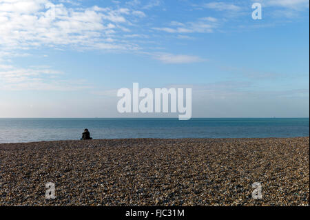 Einsame Figur sitzt auf leeren Strand, Brighton, UK Stockfoto