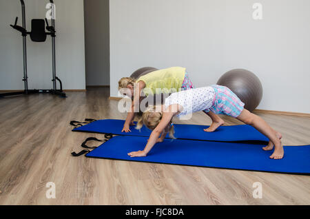 Zwei kleine blonde Mädchen in der Turnhalle mit grauen passen Kugeln und blue Matts tun Übung Stockfoto