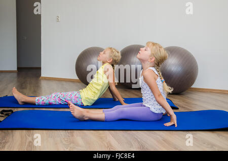 Zwei kleine blonde Mädchen in der Turnhalle mit grauen passen Kugeln und blue Matts tun Übung Stockfoto