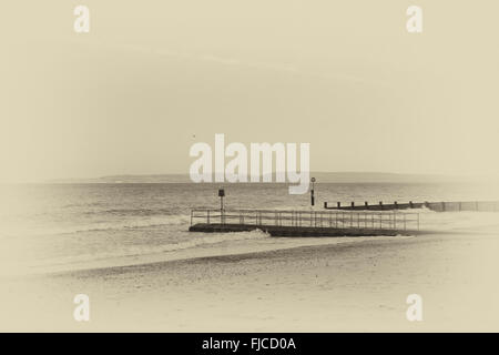 Ein schwarz-weiß Foto von einem Abendlicht ein Vogel fliegt in den Himmel auf das Meer, Blick auf einem Steg am Strand mit San getroffen Stockfoto