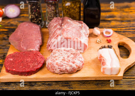 Rohes Rindfleisch und Schweinefleisch Fleischstücke auf Schneidebrett und Glas würzen Container auf Tisch im Hintergrund Stockfoto