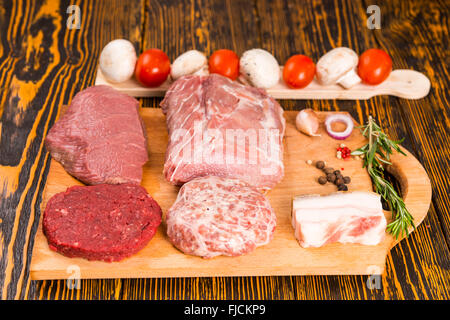 Übersichtlich Stücke rohes, rotes Fleisch und Schweinefleisch auf Schneidebrett neben Paprika, Zwiebel, Rosmarinzweig, Tomaten und Champignons Stockfoto