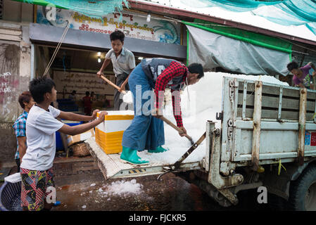 MANDALAY, Myanmar – Männer schaufeln Eis von der Rückseite eines Lastwagens in Eimer und Kühler, um es an die Fischverkäufer auf der Straße auf dem Fisch- und Blumenmarkt in Mandalay, Myanmar (Birma), zu liefern. Stockfoto