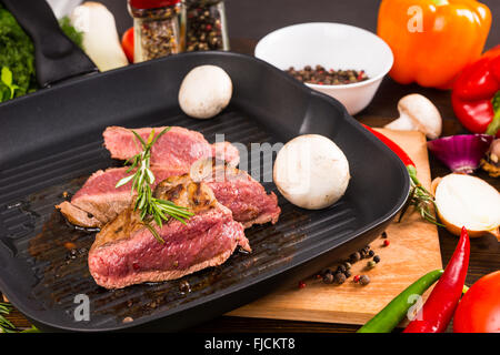 Stillleben mit seltenen Roastbeef Sizzling in heißen Eisenpfanne mit frischen Pilzen und umgeben von bunten Gemüse und Gewürze Kräuter und Gewürze hautnah. Stockfoto