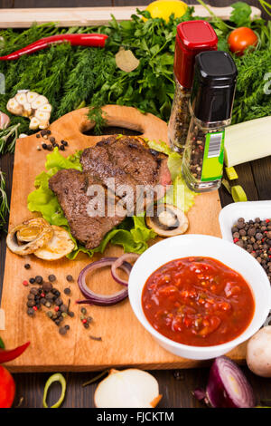 Stillleben mit gekochtem Rindfleisch auf Holzbrett mit Salsa-Dip, umgeben von frischen Kräutern, Gemüse und Gewürze Schüssel hautnah. Stockfoto