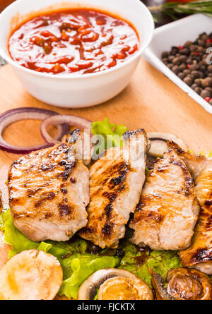 Close-up-Stillleben mit gegrilltem Schweinefleisch Koteletts ruht auf Holzbrett mit Schüssel frische Salsa-Dip, Gemüse und Pfeffer würzen. Stockfoto